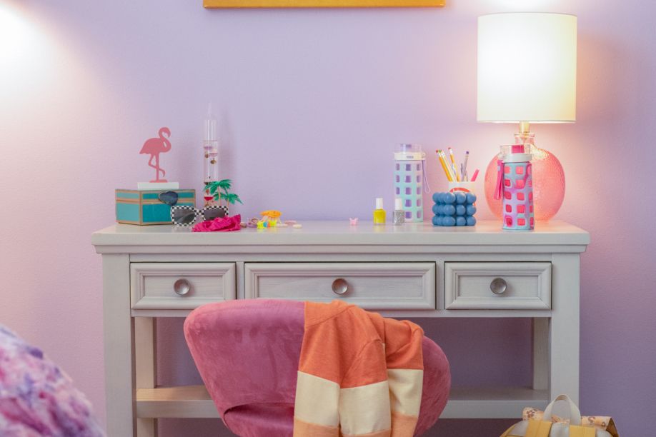A white desk with a pink chair, lamp, and various decorative items.
