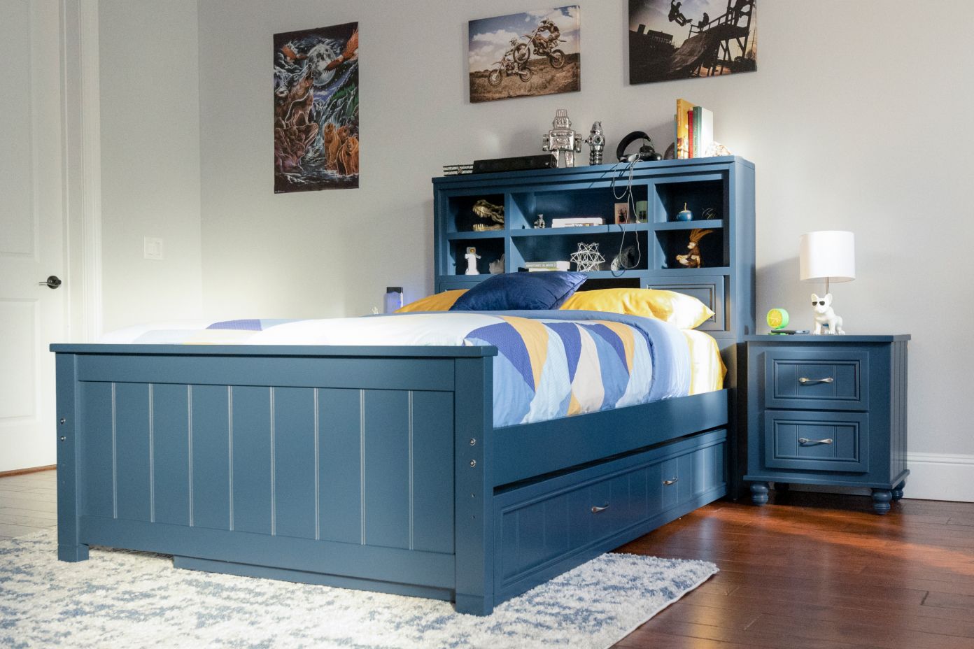 Blue bed with headboard and storage drawers, nightstand, and artwork.
