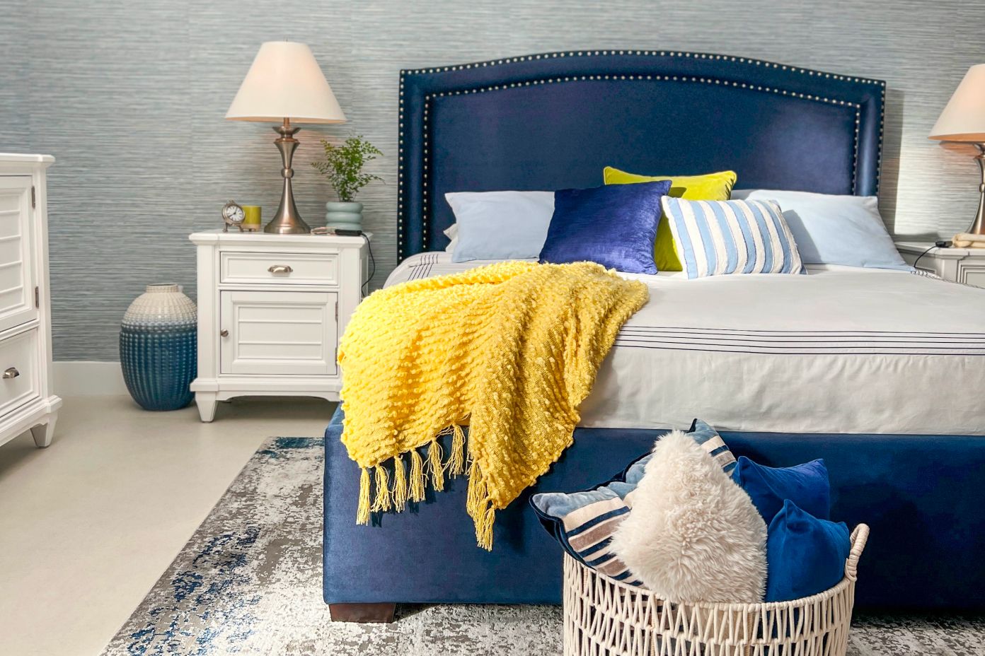 A bedroom with a blue bed, white nightstands, and a yellow throw blanket.

