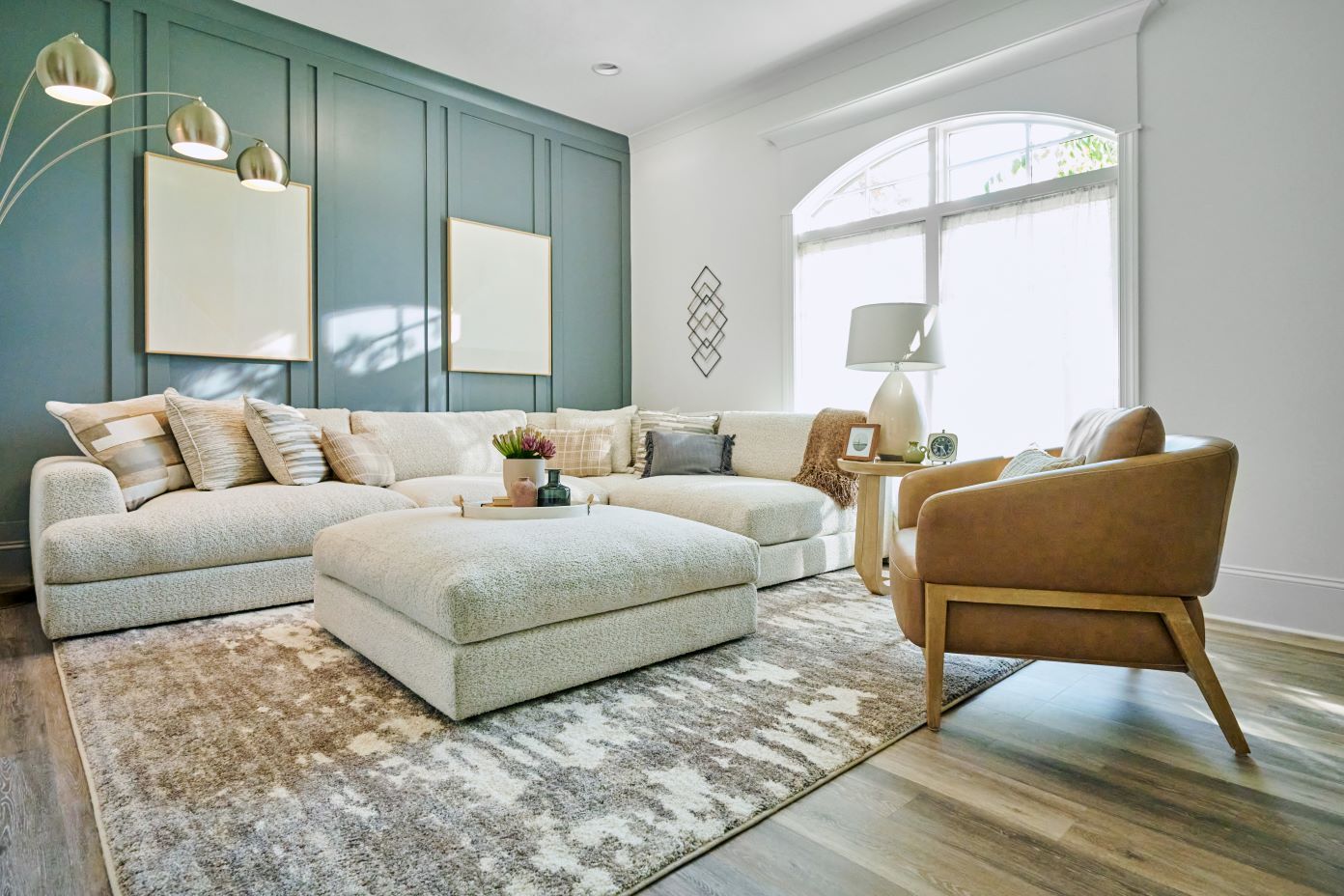 A living room with a sectional sofa, ottoman, and a brown leather armchair.
