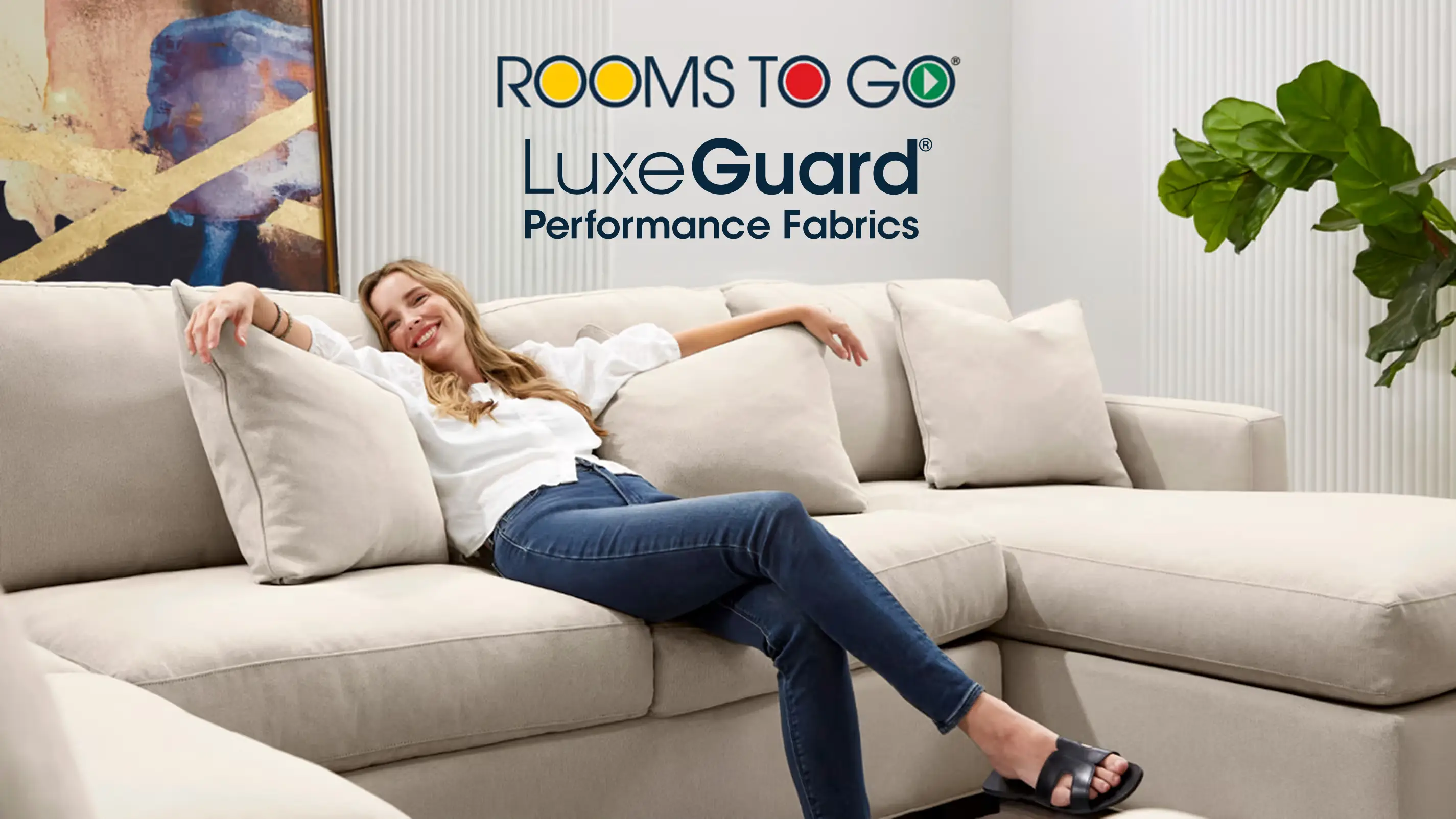 ROOMS TO GO LuxeGuard Performance Fabrics. A woman relaxes on a light-colored sectional sofa in a bright living room.