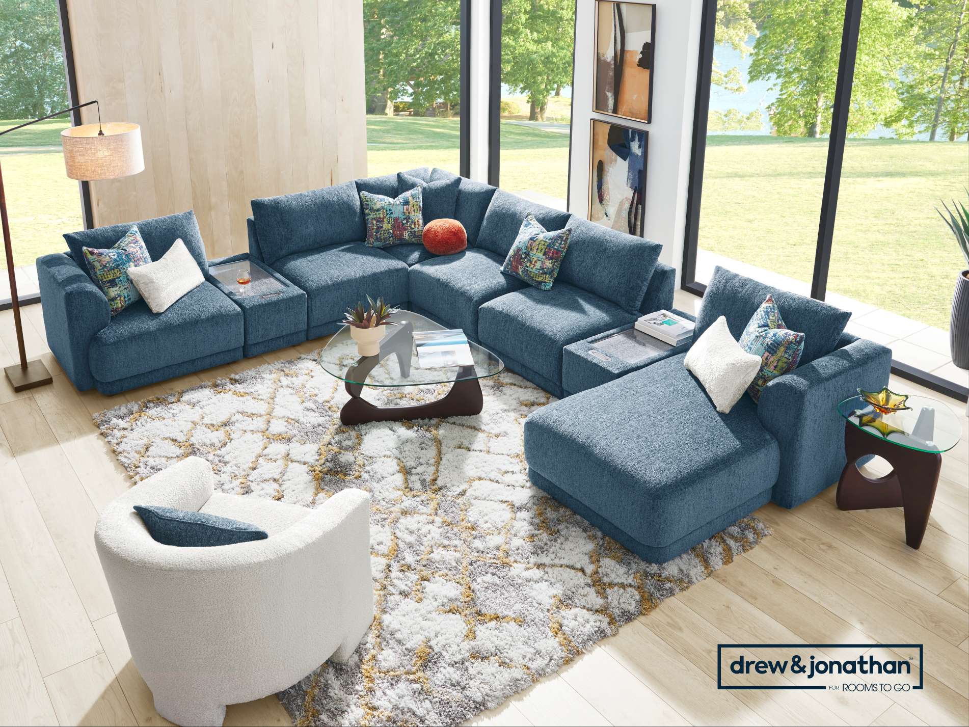 drew & jonathan for ROOMS TO GO. A blue sectional sofa with a white chair and a rug.
