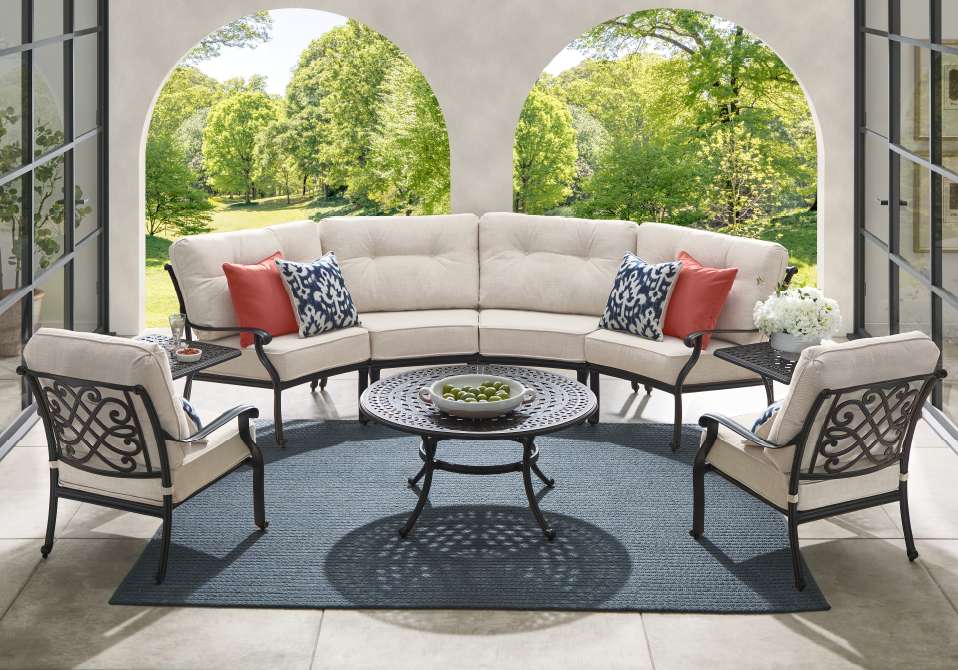 Outdoor patio furniture set with a sectional sofa, armchairs, and a coffee table on a blue rug.
