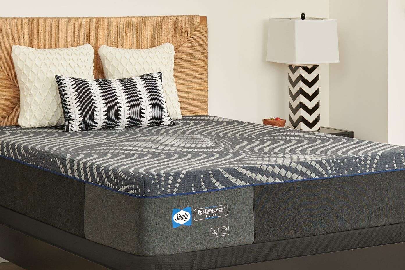 Sealy Posturepedic Plus mattress on a bed with pillows and a lamp.
