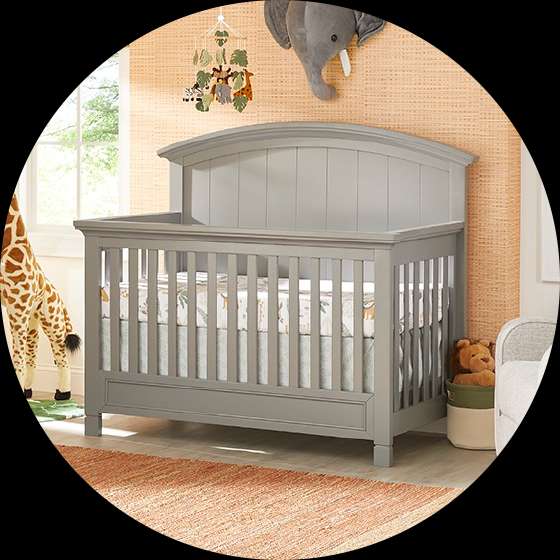 A gray crib in a nursery with a giraffe and elephant decor.
