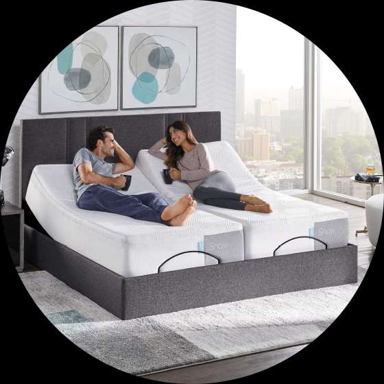 A couple relaxing on an adjustable bed, holding mugs. The bed has a "Snow" label.
