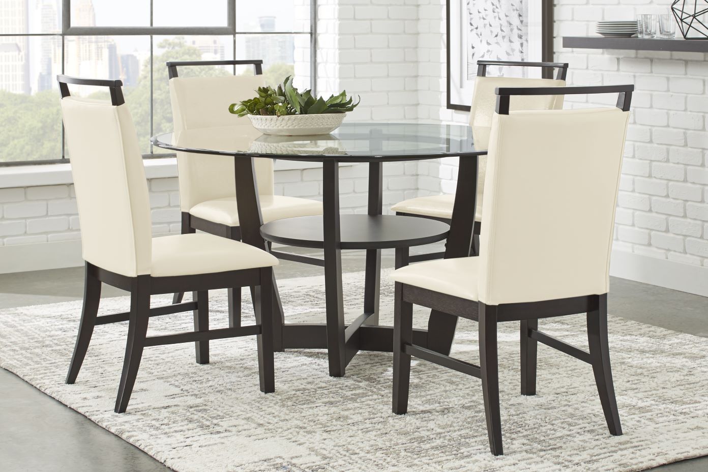 Dining table with four chairs. The table has a glass top and dark wood base. The chairs have cream-colored seats and dark wood frames.
