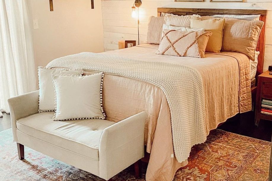 brown bedframe with light covers and a white accent bench