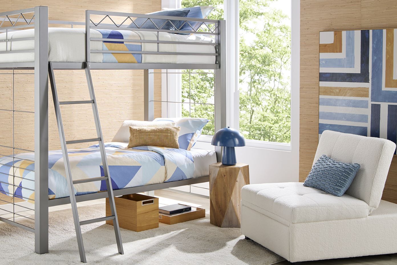 A metal bunk bed with blue and yellow bedding, a white chair, and a blue lamp.
