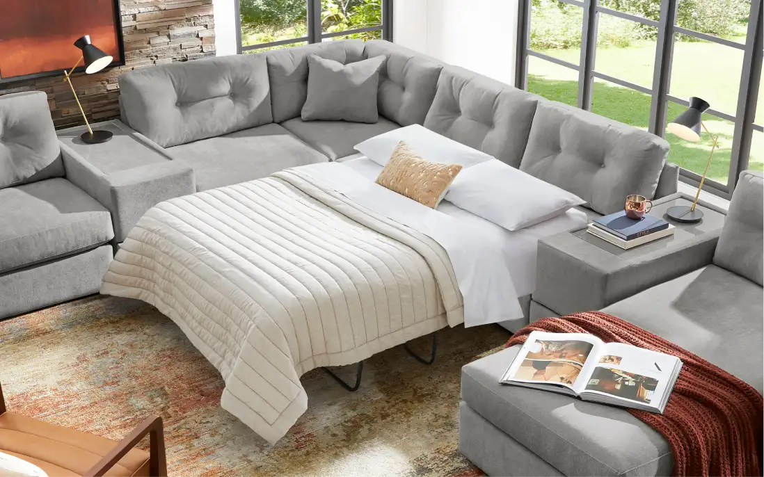 Gray sectional sofa with a pull-out bed, pillows, and a blanket.
