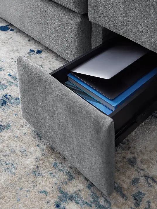 A gray sofa with a pull-out drawer containing a laptop and books.
