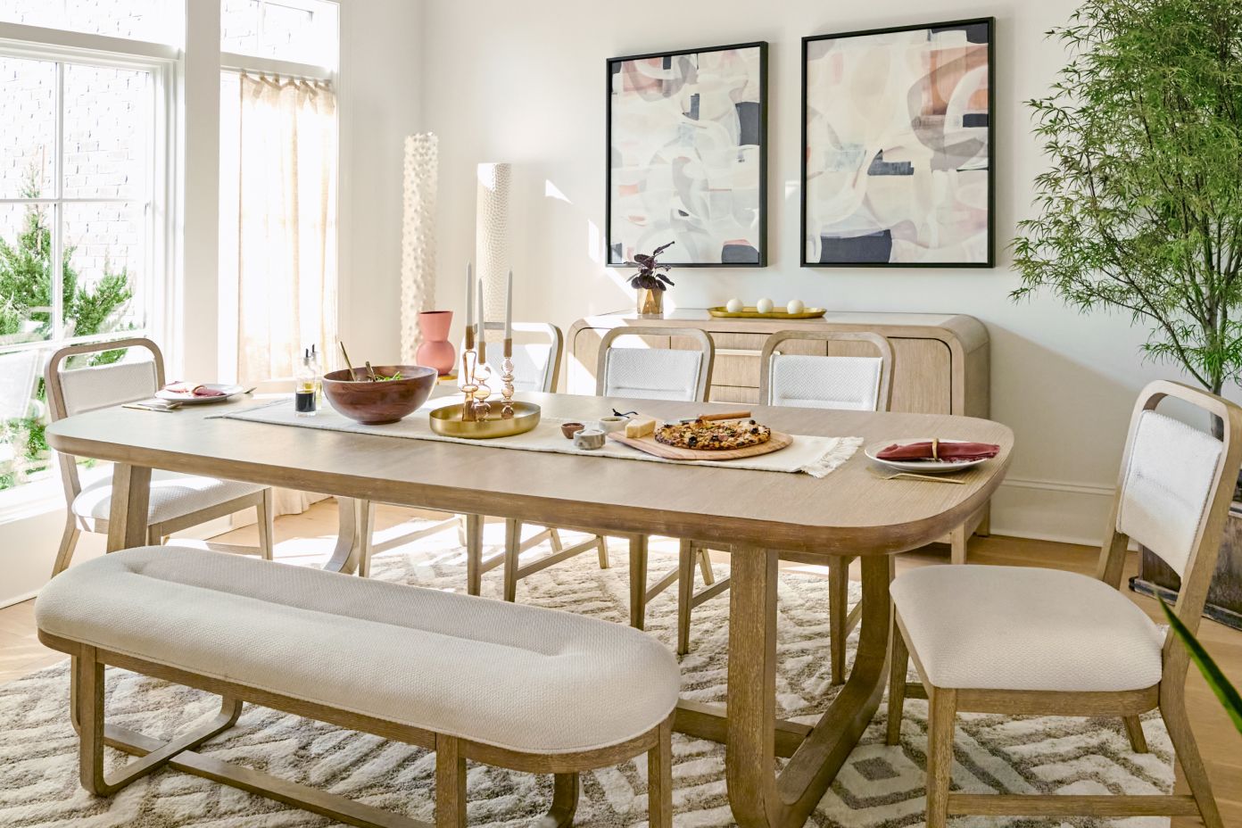 Dining room with a wooden table, chairs, and a bench. Artwork hangs on the wall.
