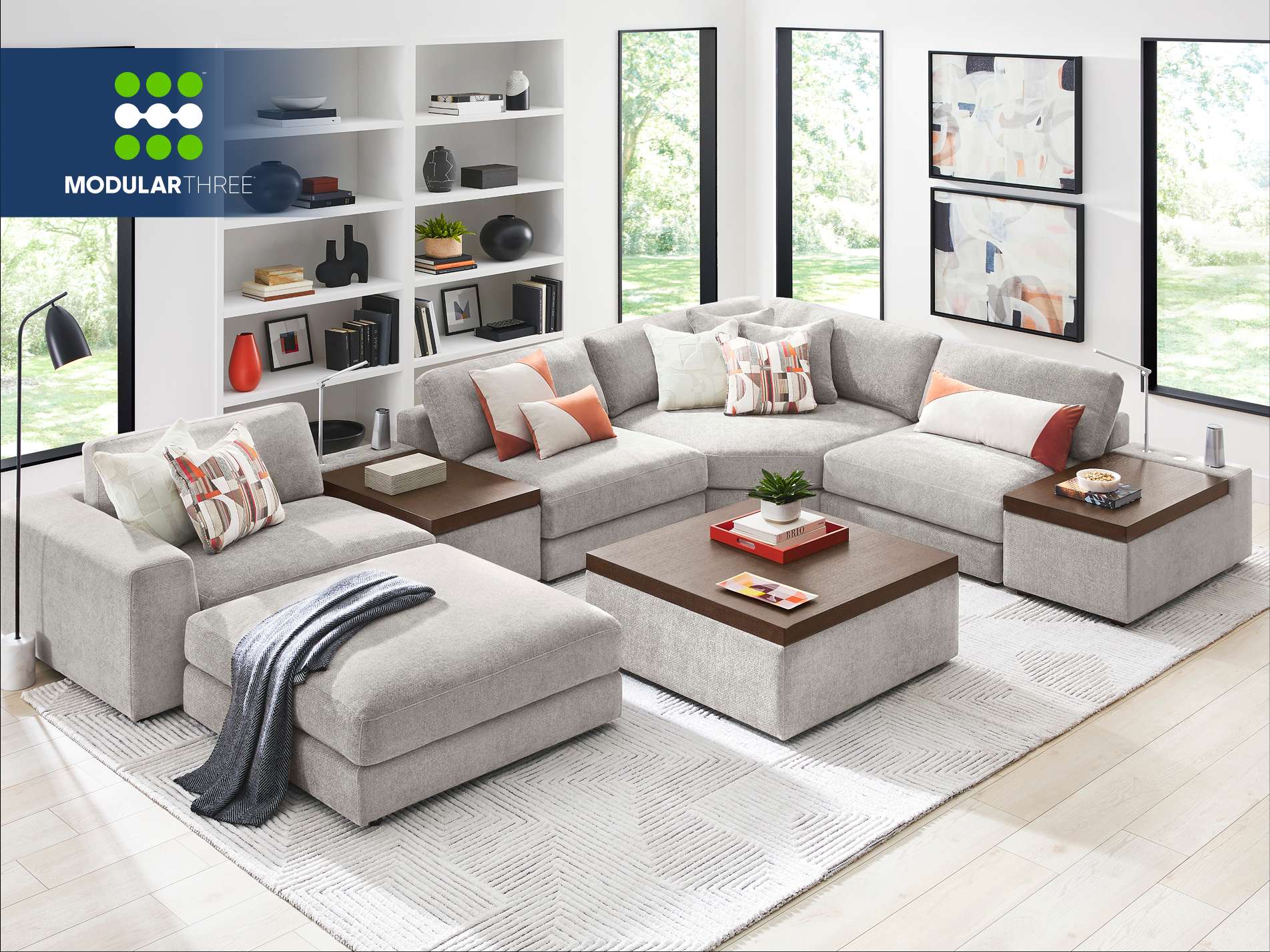 MODULAR THREE. A modern gray sectional sofa with ottomans and a coffee table in a living room.

