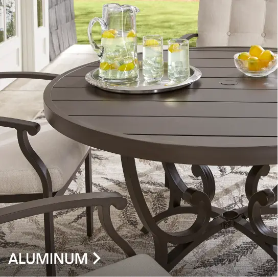 ALUMINUM. A round, dark brown metal patio table with chairs and a pitcher of lemonade on a patterned outdoor rug.