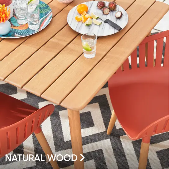 NATURAL WOOD. A wooden outdoor dining table with two red chairs on a patterned rug.