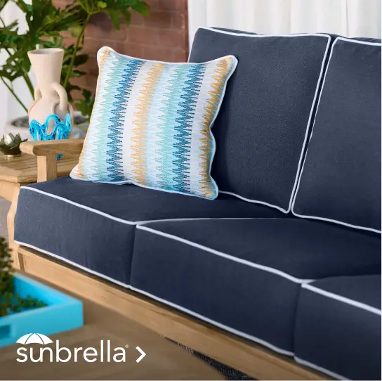 Sunbrella logo on a navy blue outdoor sofa with a patterned accent pillow and wooden frame.