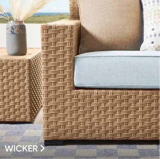 WICKER. A close-up of a wicker outdoor sofa with light blue cushions and a matching side table on a checkered rug.
