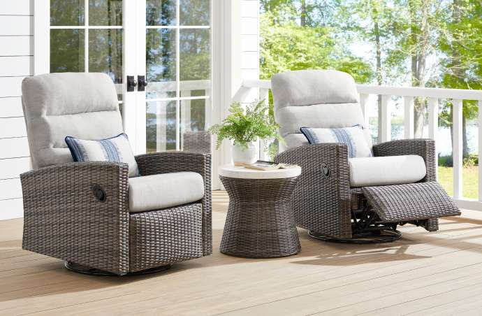 Two gray wicker outdoor recliner chairs with white cushions and a small side table.