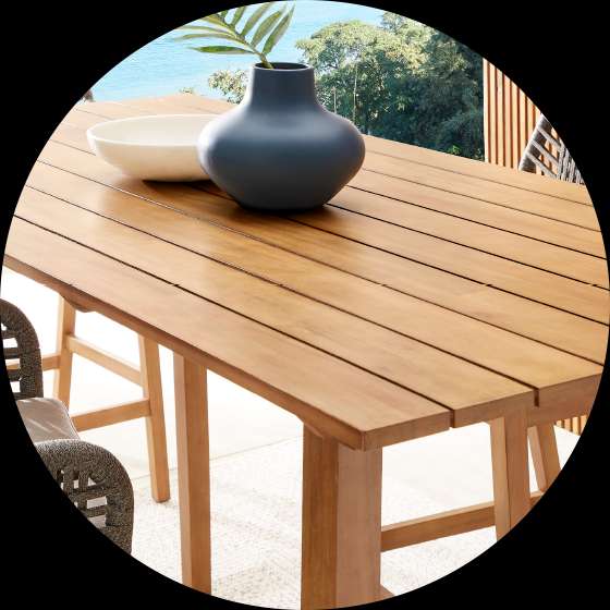 Wooden outdoor dining table with a blue vase and a white bowl.
