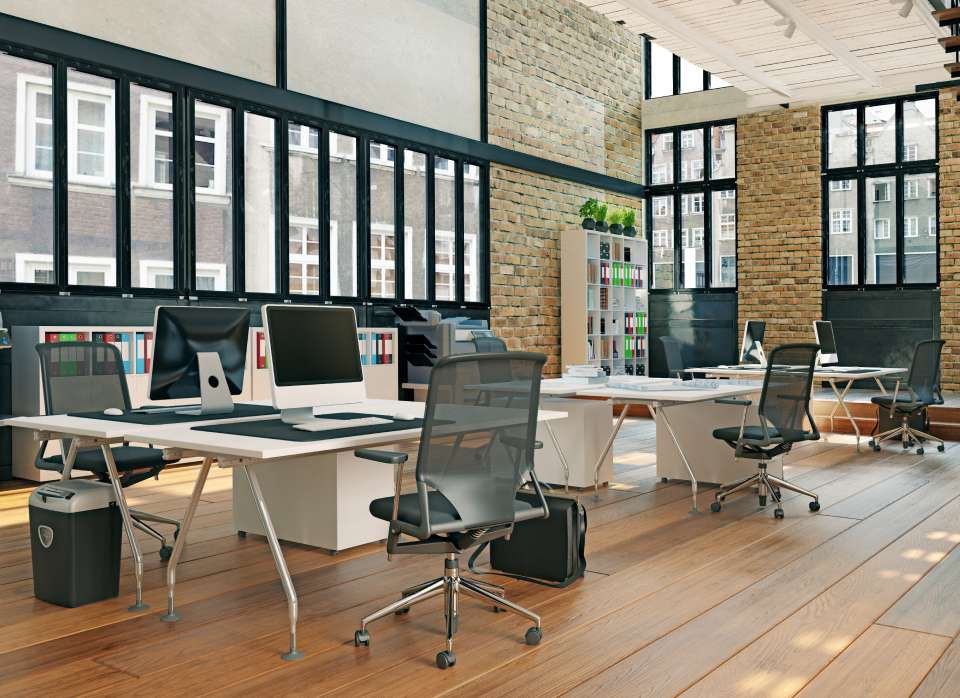 An office with desks, chairs, computers, and brick walls.
