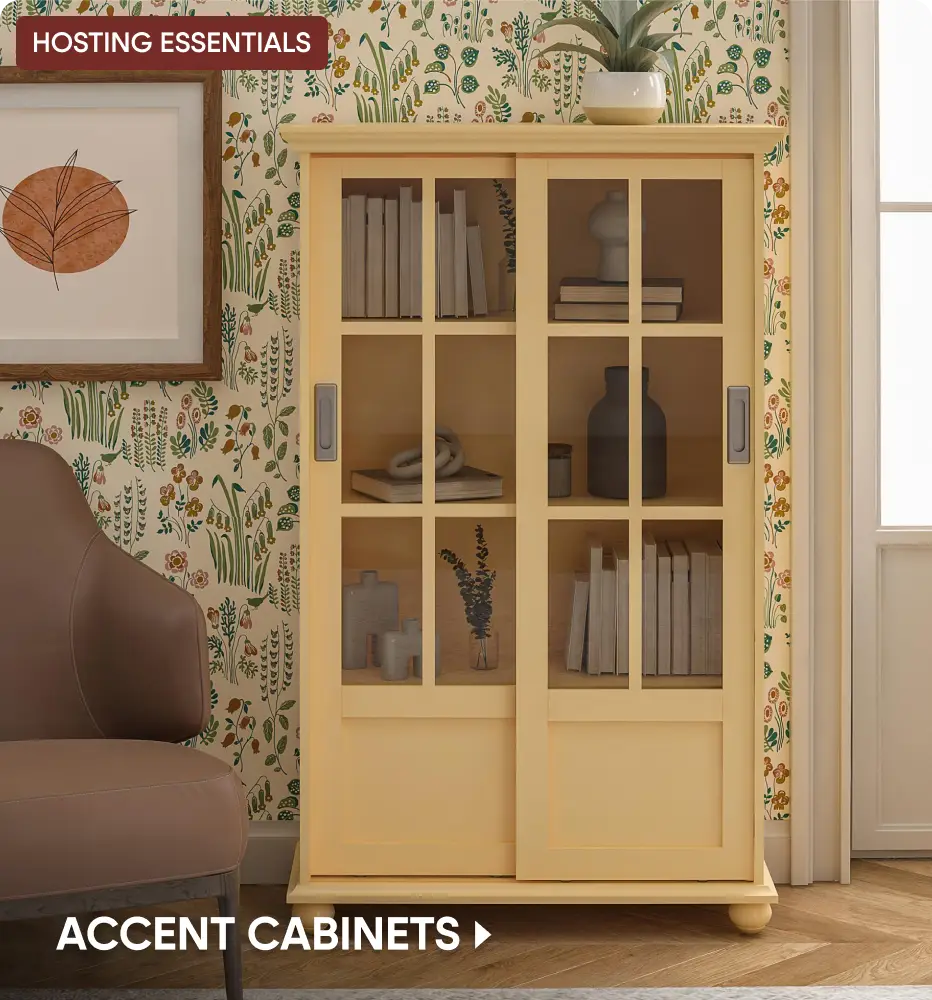 HOSTING ESSENTIALS ACCENT CABINETS: A light yellow wooden cabinet with sliding glass doors, styled with books and decor.