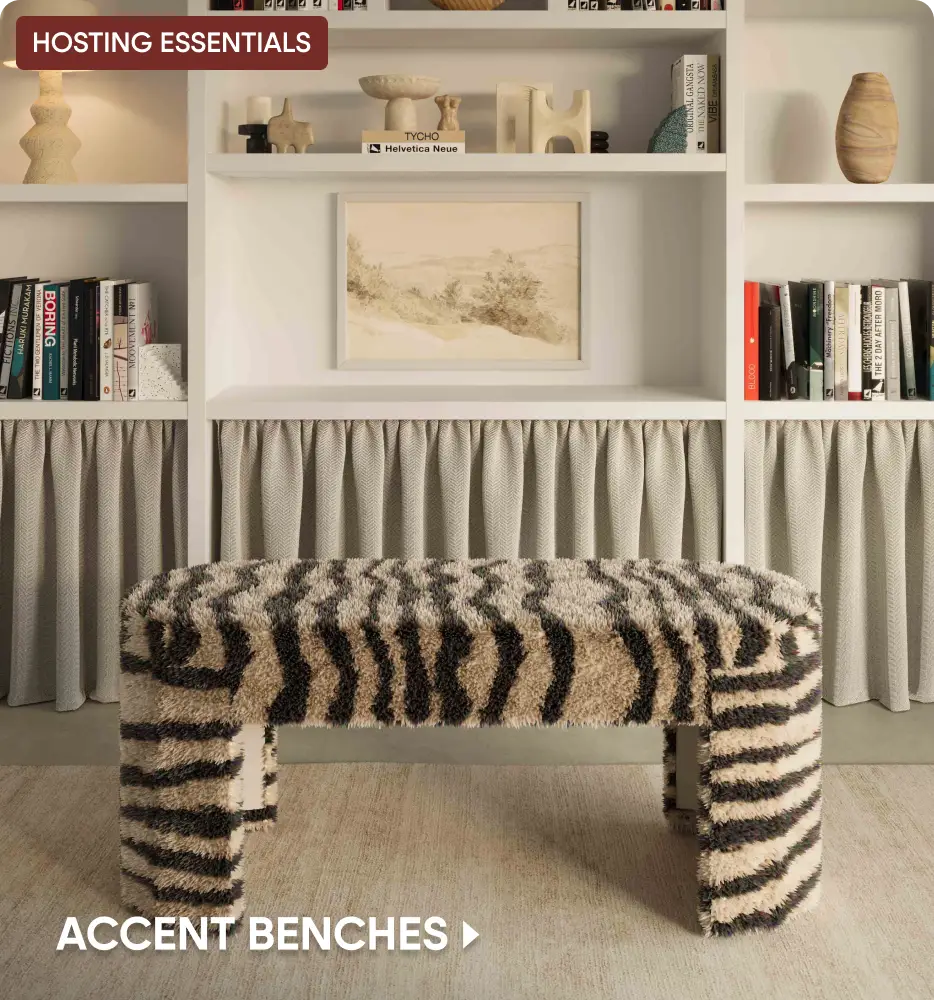 HOSTING ESSENTIALS ACCENT BENCHES. A shaggy, zebra-print bench sits in front of a bookshelf with a curtained base.