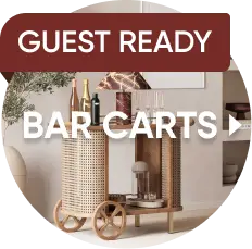 GUEST READY BAR CARTS. A wooden bar cart with cane detailing, wheels, and glassware in a modern room.