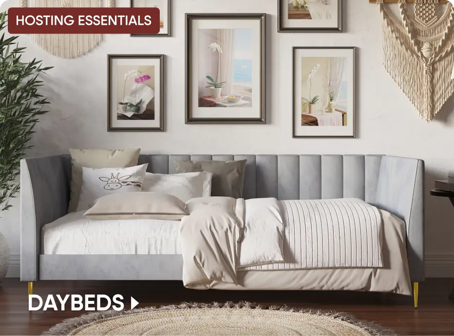 HOSTING ESSENTIALS DAYBEDS. A light blue upholstered daybed with gold legs in a room with framed art and a macrame wall hanging.