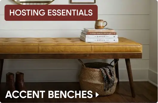 HOSTING ESSENTIALS ACCENT BENCHES. A tufted tan leather bench with a wooden frame, styled with books and a woven basket.