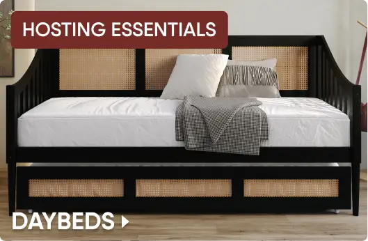 HOSTING ESSENTIALS DAYBEDS: A black wooden daybed with cane paneling, a white mattress, and decorative pillows.