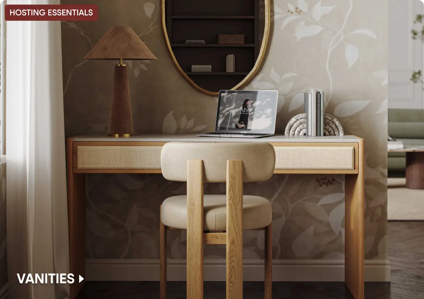 HOSTING ESSENTIALS VANITIES: A modern wooden desk with a cream-colored chair, lamp, laptop, and books against floral wallpaper.