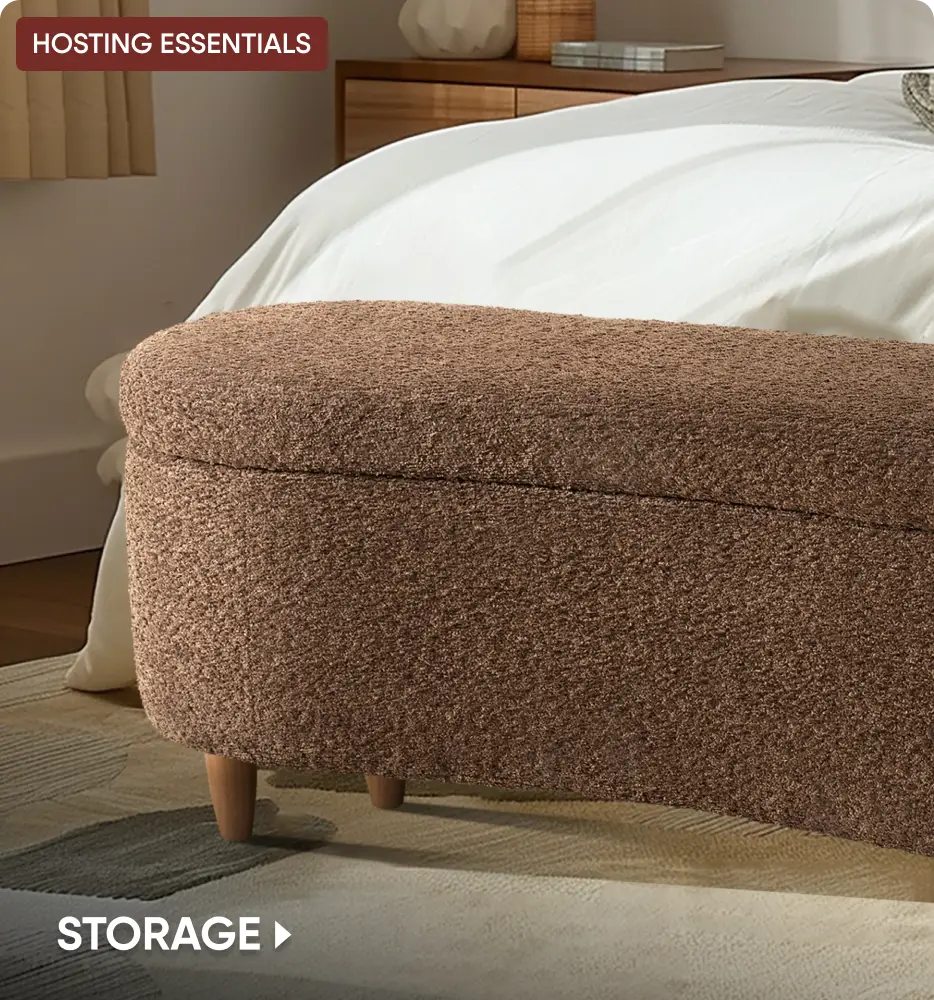 HOSTING ESSENTIALS STORAGE. A brown, textured, oval-shaped storage bench sits at the foot of a bed.