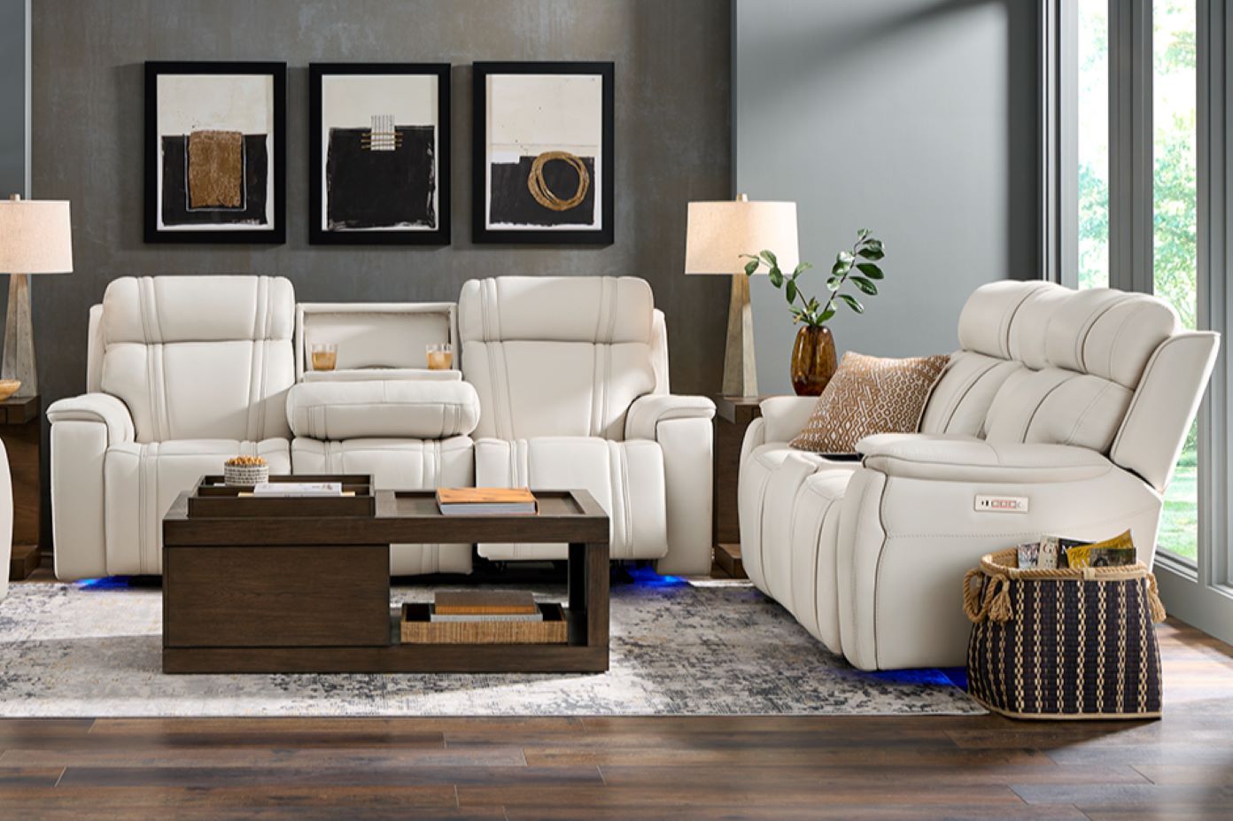 White leather reclining sofa and chair set with a dark wood coffee table and abstract art.
