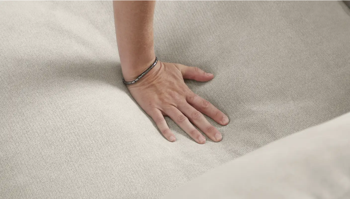 A hand pressing down on a light-colored, textured fabric.