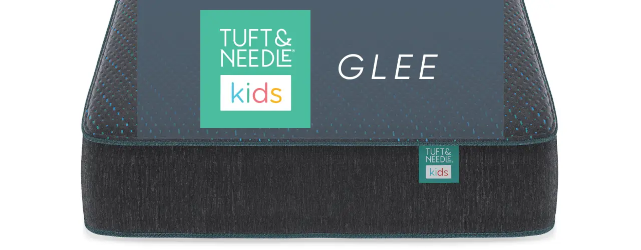 Tuft & Needle Kids Glee mattress with a dark grey and blue textured cover and branding label.