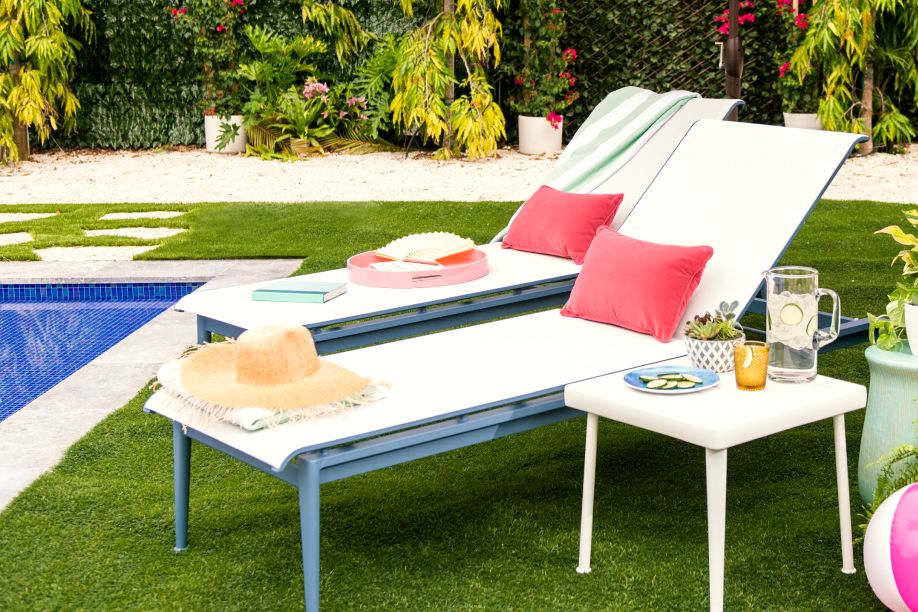 Two white lounge chairs with red pillows, a small table with drinks, and a straw hat.
