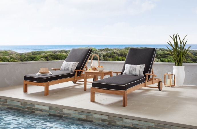 Two black cushioned lounge chairs on a patio overlooking the ocean.
