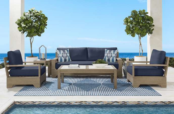 Outdoor furniture set with a sofa, two chairs, and a coffee table on a blue rug.
