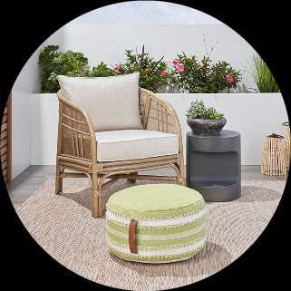 Rattan armchair with cushion, green ottoman, and side table on a patio.
