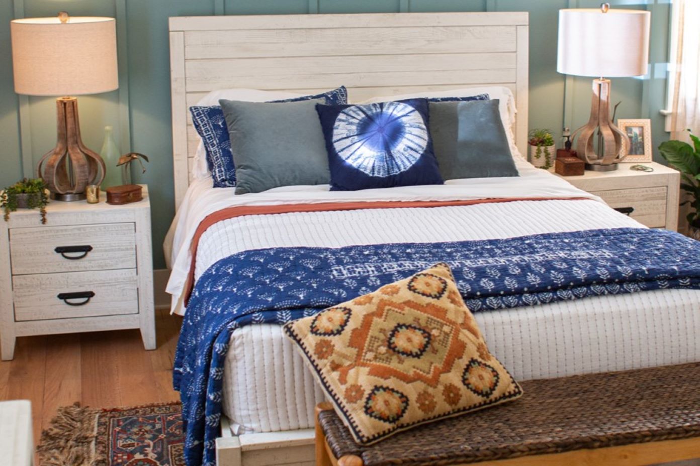A bedroom with a white bed, blue bedding, and two nightstands with lamps.

