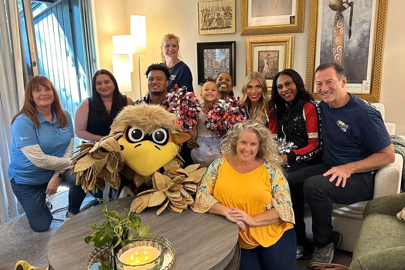A group of people pose with a mascot in a living room.
