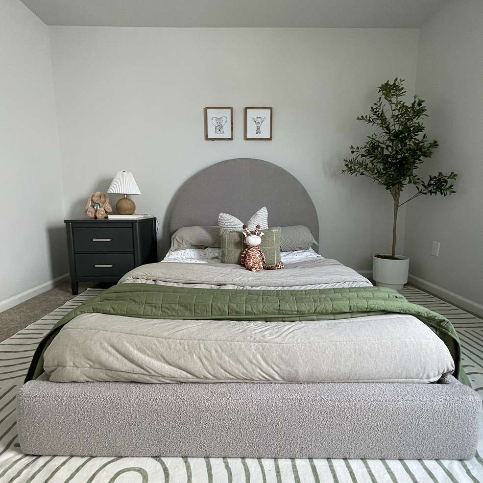 A child's bedroom with a bed, nightstand, and a small tree.
