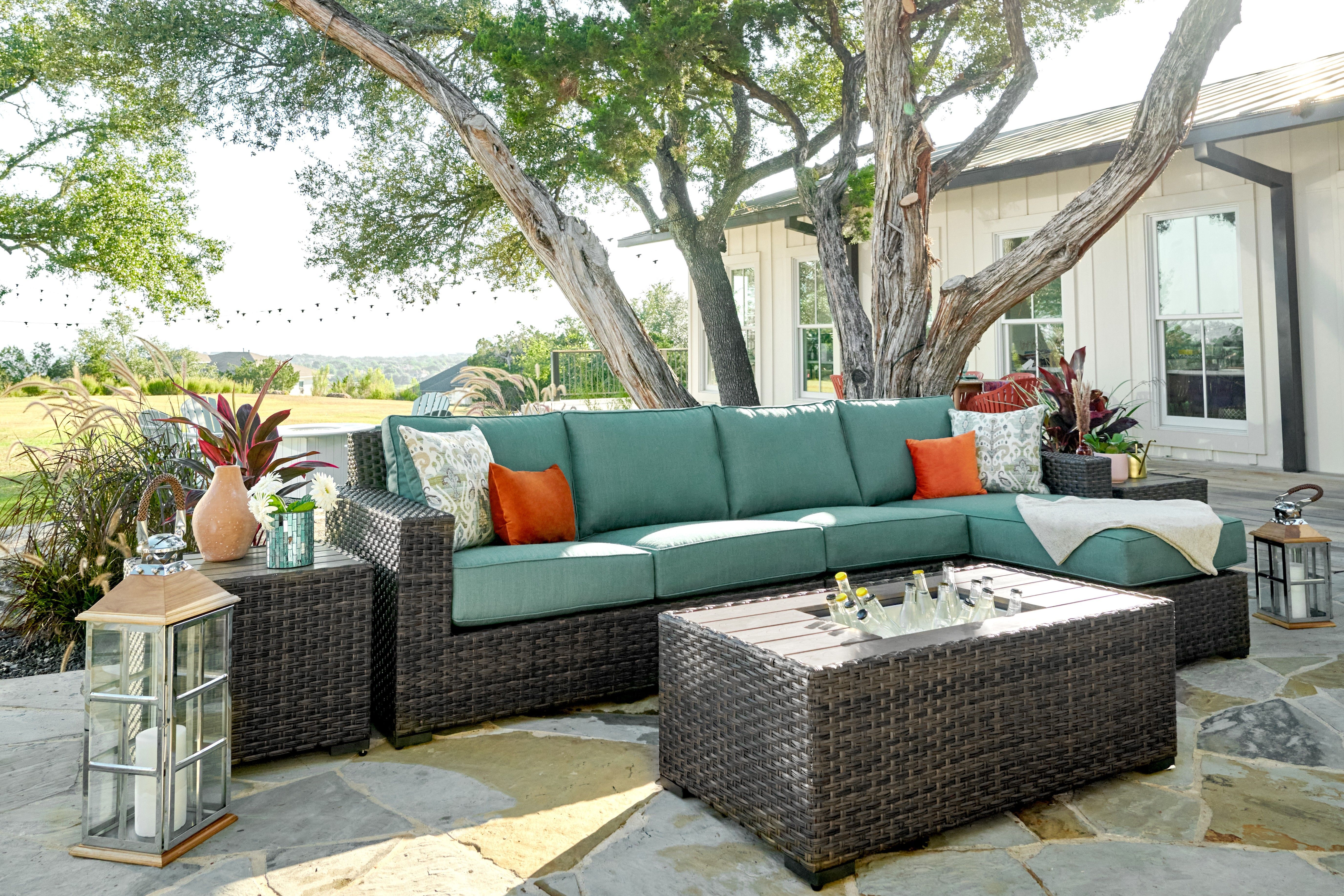 Outdoor sectional sofa with teal cushions, orange pillows, and a woven coffee table with drinks.
