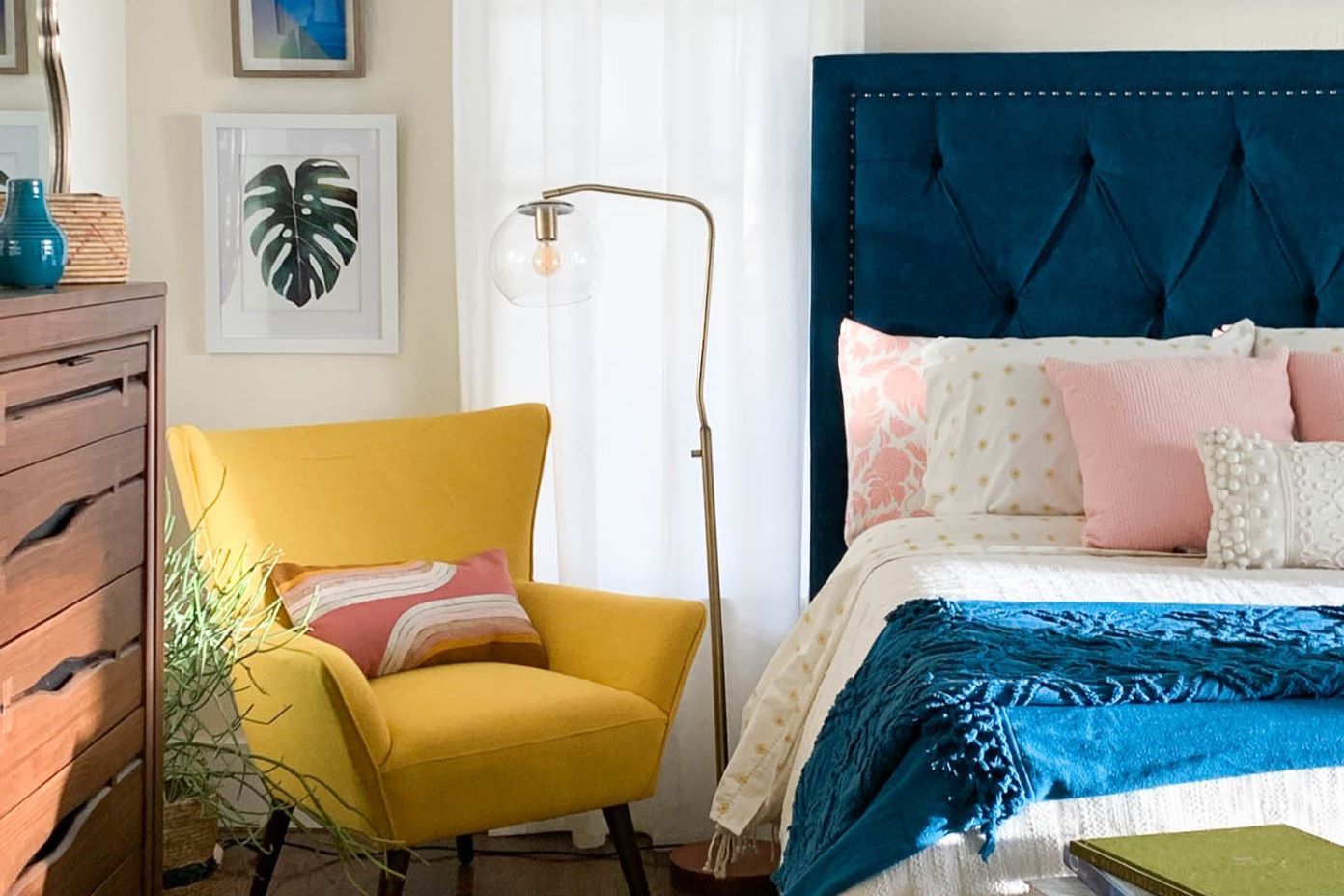 A bedroom with a yellow chair, blue headboard, and a floor lamp.
