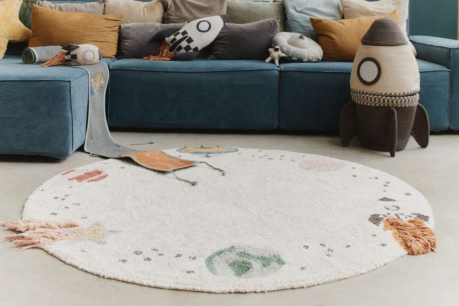 A round rug with a space theme, a blue couch, and rocket-shaped toys.
