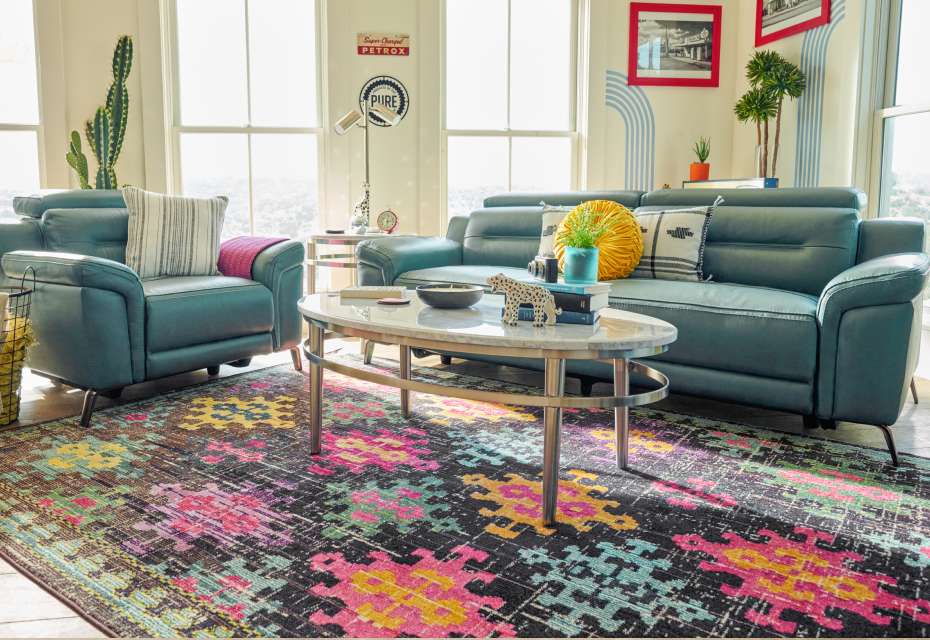 A living room with teal leather furniture, a colorful rug, and a marble coffee table.

