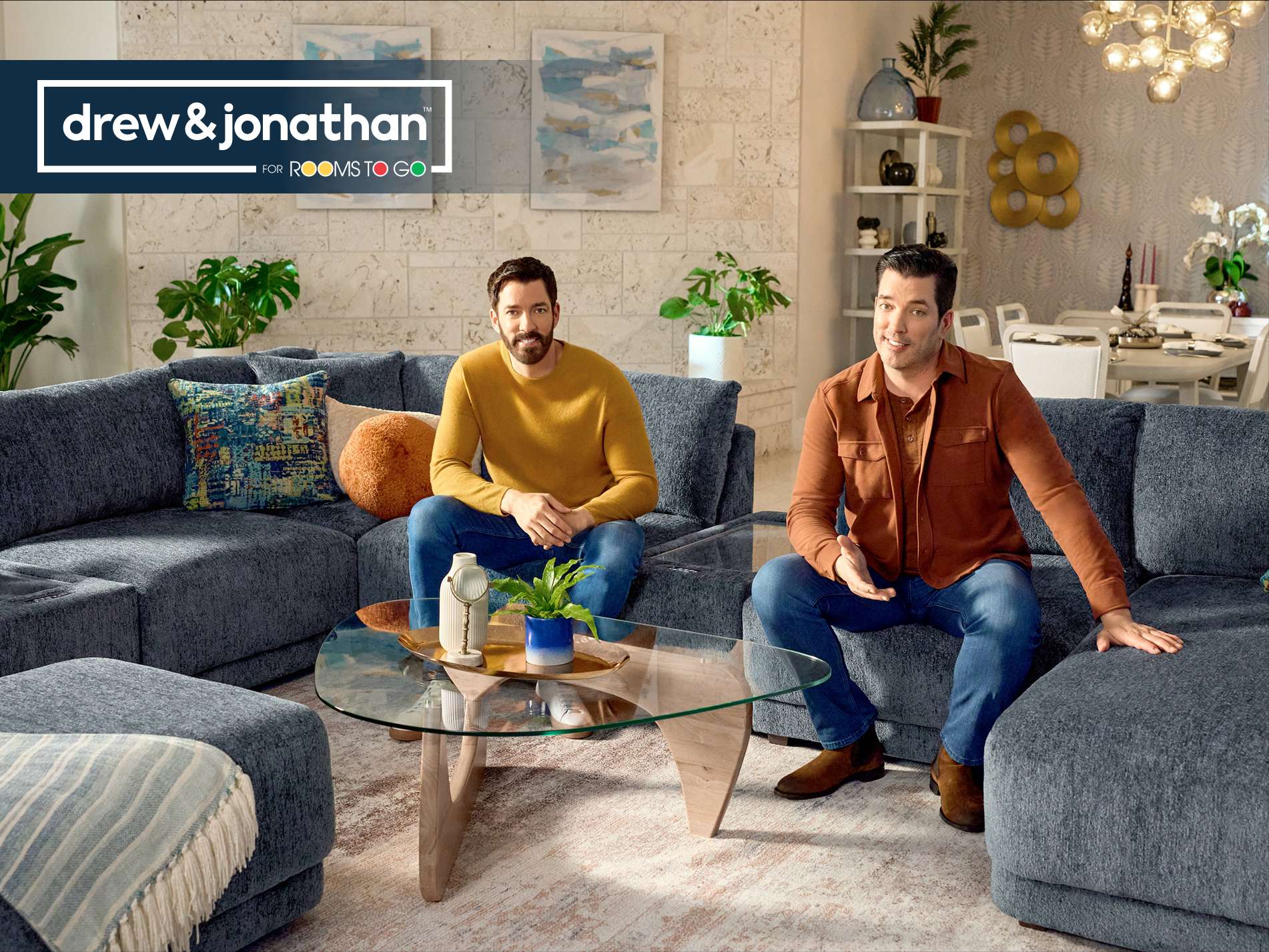 drew & jonathan for Rooms To Go. Two men sitting on a gray sectional sofa.
