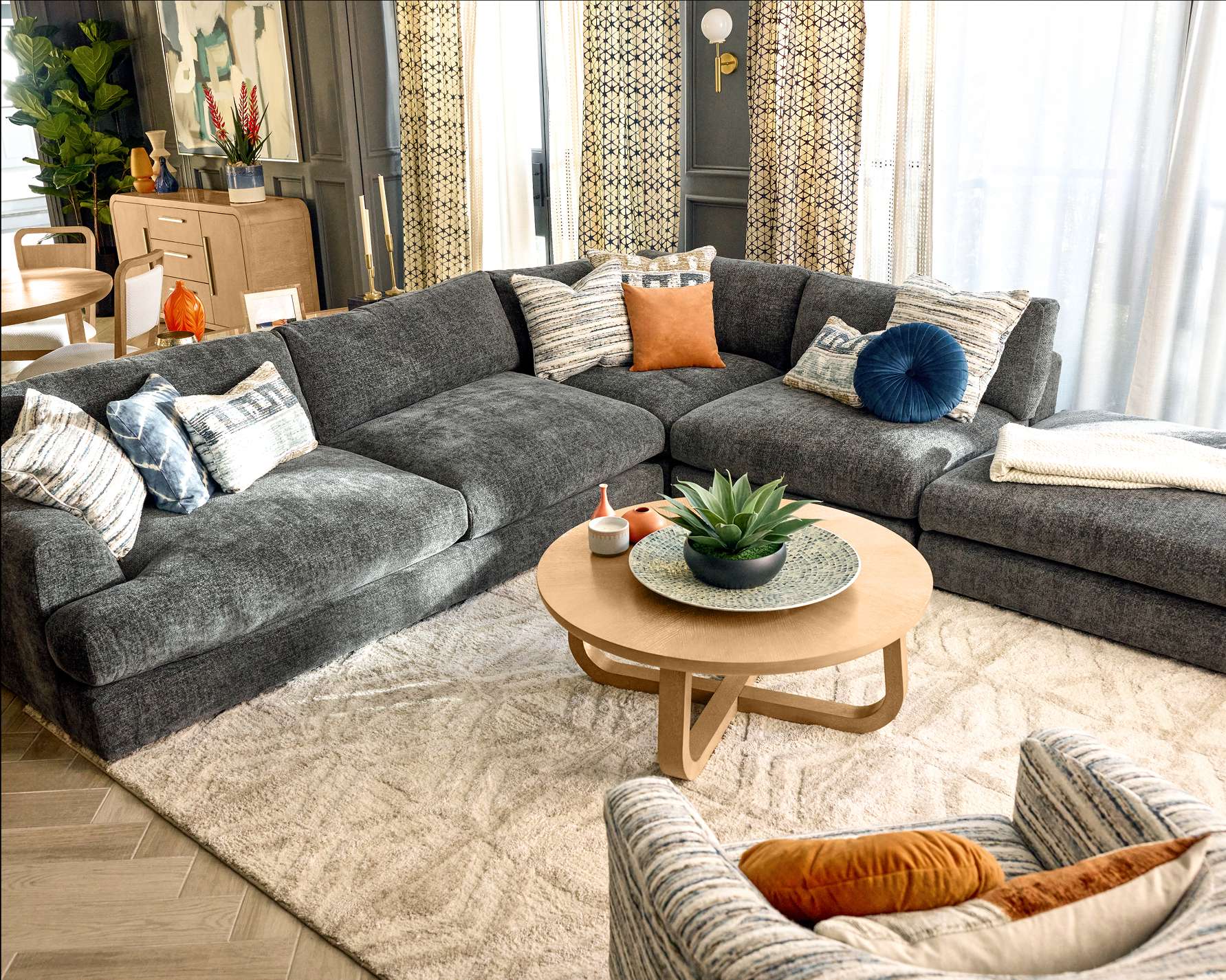 A modern living room with a gray sectional sofa, a round wooden coffee table, and a patterned rug.
