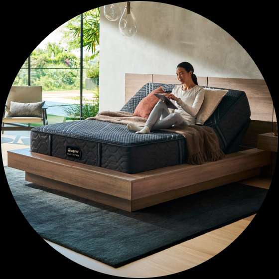 Beautyrest Black Series mattress. A woman sits on the bed using a tablet.
