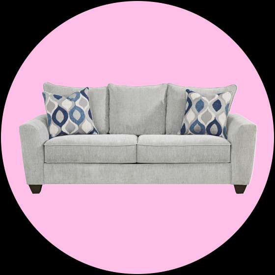 Gray loveseat with two patterned pillows on a pink background.

